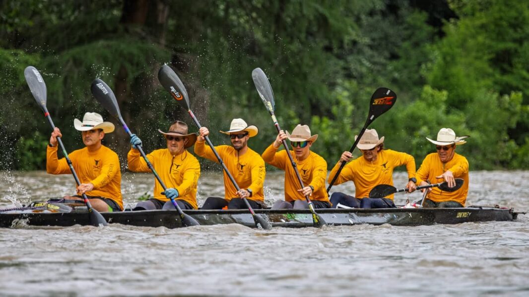 Six person canoe team in straw cowboy hats paddling hard on a Texas river