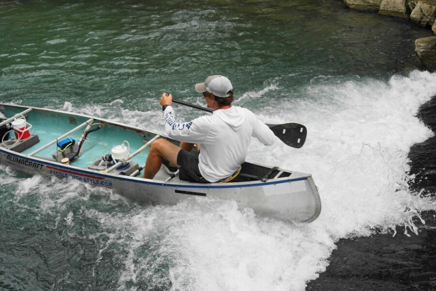Spencer Fuller running whitewater rapids in an aluminum canoe on a Texas river
